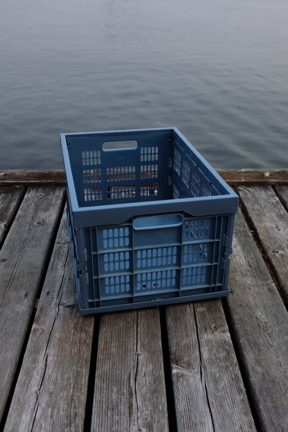 Large blue folding plastic crate sitting on a wooden dock right next to the water.