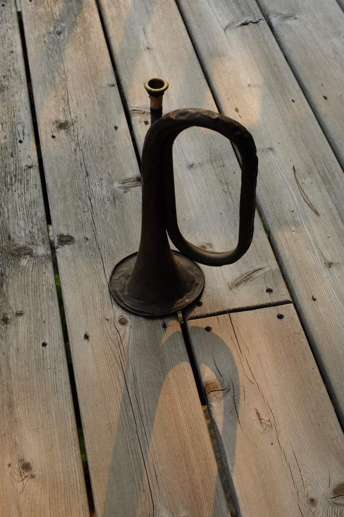 Old dented bugle on a wooden deck, sun behind it casting a long shadow.