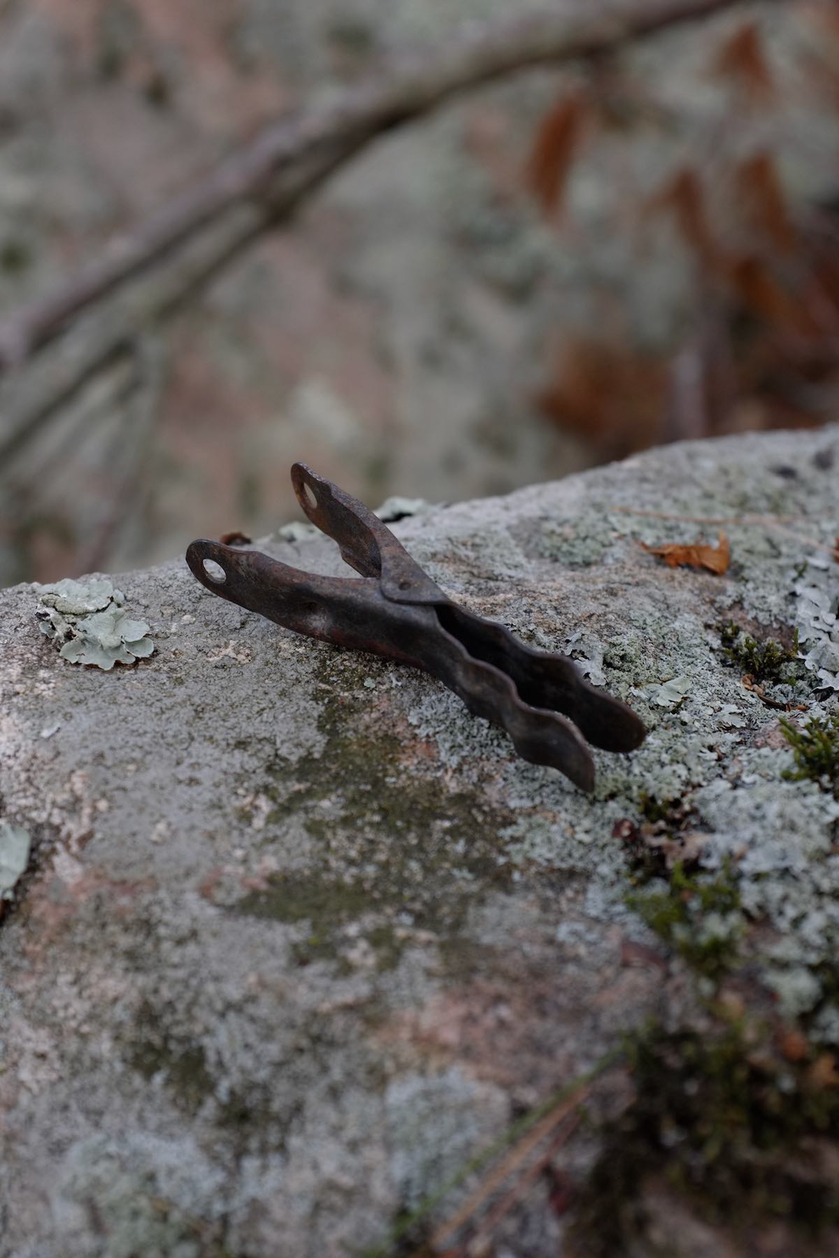 The same type of clothespeg, entirely burnt but not deformed, missing its spring. It sits on a lichen-covered granite outcropping.