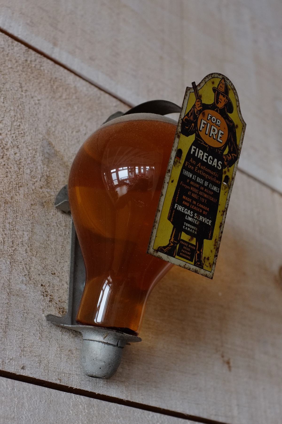 What appears to be a lightbulb full of amber liquid. It's held by a metal wall bracket, the front of which has an image of a firefighter and text explaining the use of the fire-gas product.