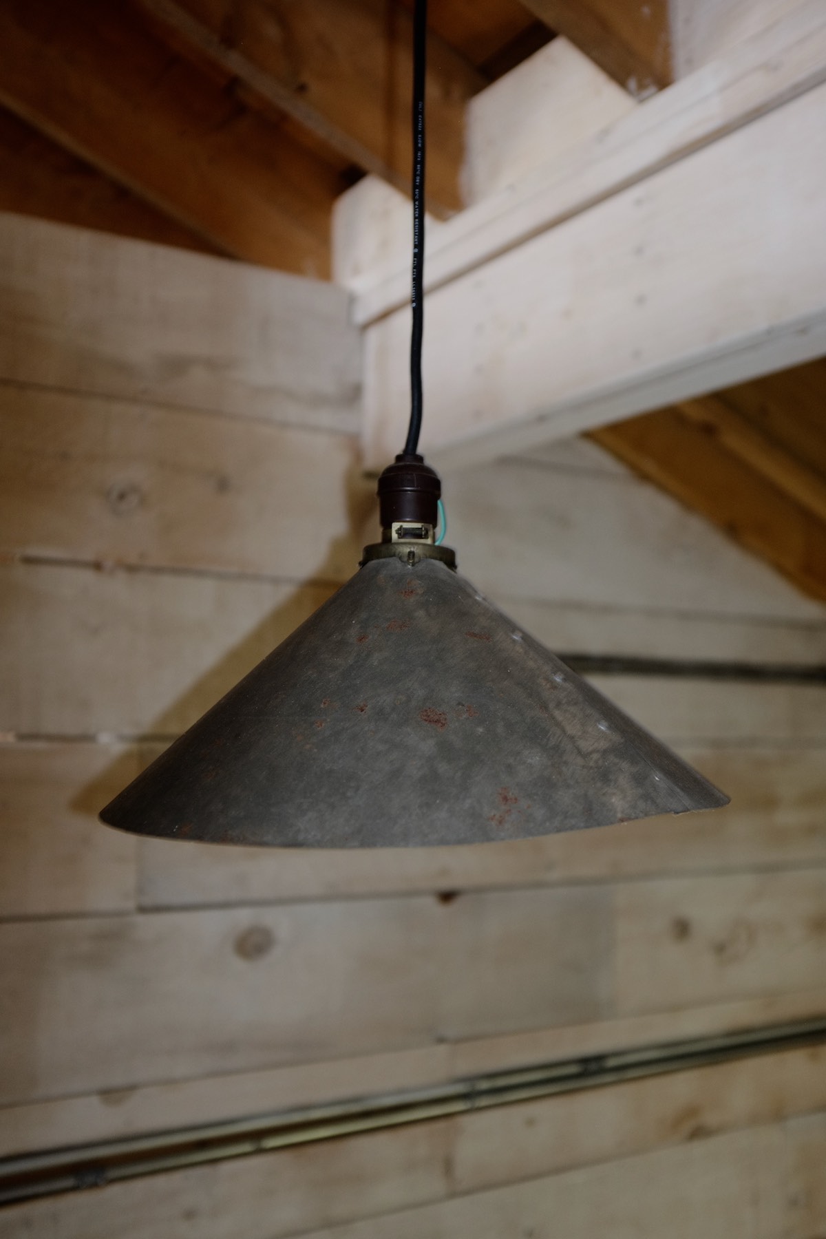 Flash photo of a tin cone-shaped lampshade hanging from a wooden ceiling.