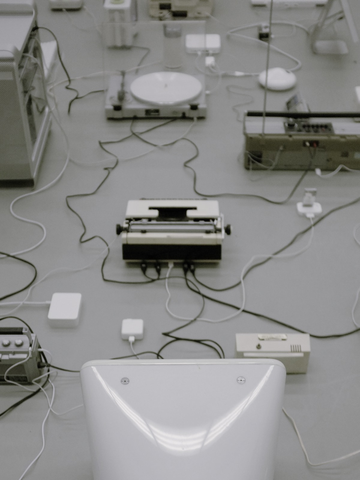 Back view of aforementioned machine installation, rear sides of turntable, cassette boombox, typewriter, and Apple eMac prominent.